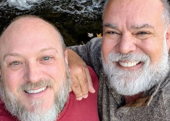 Two men stand in front of a cascade and smile at the camera.