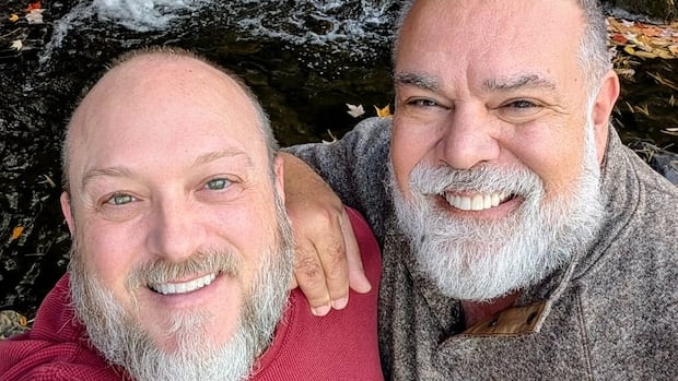 Two men stand in front of a cascade and smile at the camera.