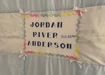 A blue and white baby blanket embroidered with the name "Jordan River Anderson."