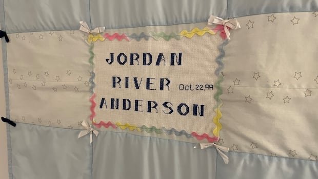 A blue and white baby blanket embroidered with the name "Jordan River Anderson."
