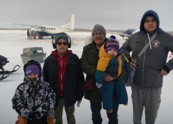 And older woman and four children standing outside at an airport.