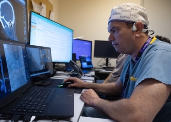 A doctor looks at a computer screen, hand on the mouse.