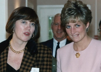 Two women walk down a hallway, with a crowd of people behind