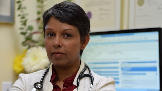 A short-haired woman in a lab coat with a stehoscope around her neck sits facing away from a computer