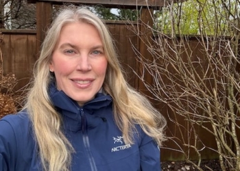 A woman with blonde hair and a navy rain jacket poses for a photo outside.