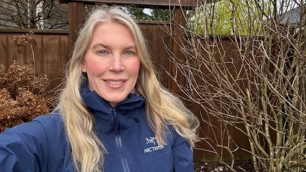 A woman with blonde hair and a navy rain jacket poses for a photo outside.