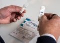 a close up of a man's hands holding a vile of liquid in his left hand and a small self testing kit for HIV in his right hand