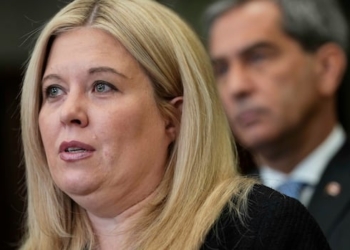 A close of of Garner standing at a podium, listening to a question from a reporter