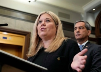 A woman speaks at a lectern while a man stands behind her.
