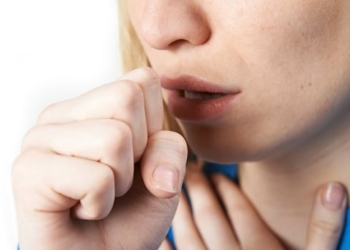 A woman coughing shields her mouth with her fist.