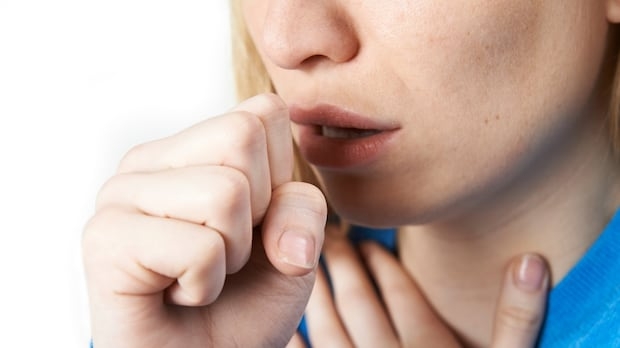 A woman coughing shields her mouth with her fist.