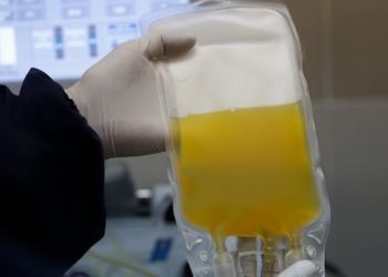 Gloved hands hold up a bag filled with yellow liquid.