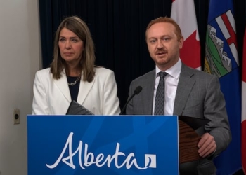 Two people at a podium with flags behind them.