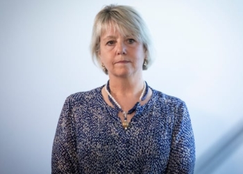 A white woman with short blond hair looks on, while wearing blue.