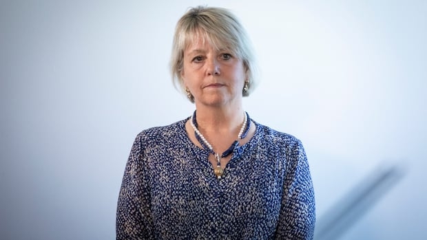 A white woman with short blond hair looks on, while wearing blue.