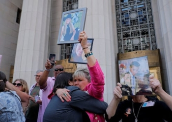 A crowd of people standing outside a courthouse embrace as they hold up images of young people in frames and on their cellphones.