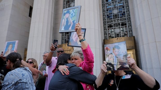 A crowd of people standing outside a courthouse embrace as they hold up images of young people in frames and on their cellphones.