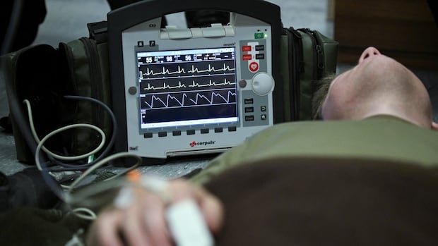 An electrocardiogram instrument (ECG) stands next to a simulated casualty during a first aid drill.