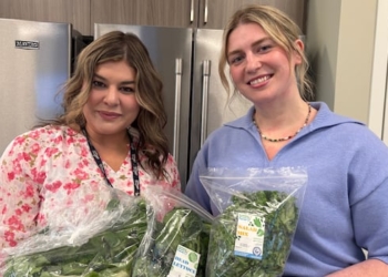 Two women hold bags of lettuce, kale and bok choy.
