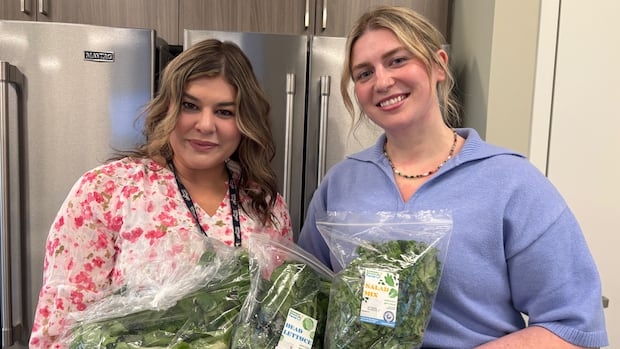 Two women hold bags of lettuce, kale and bok choy.