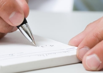 Close up of hand holding a pen writing on a prescription pad.