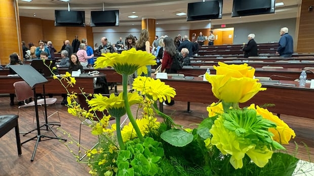 A lecture hall with wooden desks. A vase of yellow flowers with greenery sits in the foreground.