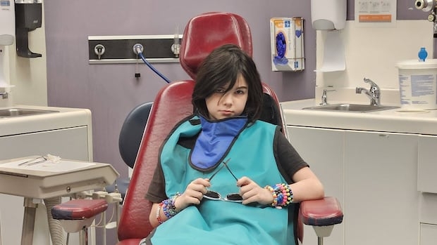 A child with shoulder length brown hair sits in a dentist chair.