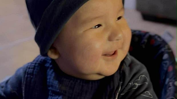 A smiling, chubby baby of about 10 months, wearing a blue hat