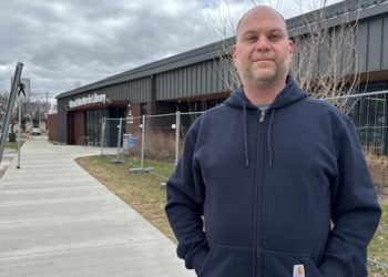 A man wearing a blue sweater is outside a building.