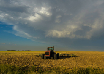 A tractor is parked in a field. Dark clouds are moving overhead.