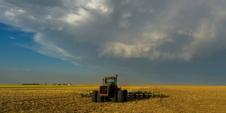 A tractor is parked in a field. Dark clouds are moving overhead.
