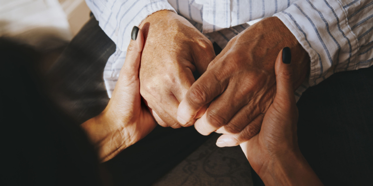 A woman holds the hands of a senior man.
