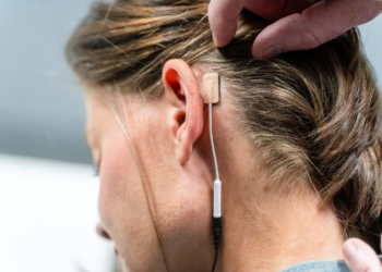 A small gel electrode with a cord is seen placed behind a woman's ear.