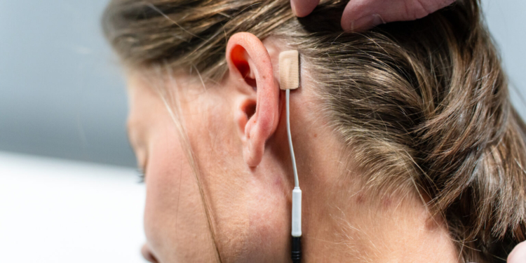 A small gel electrode with a cord is seen placed behind a woman's ear.