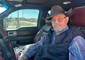 An older man wearing a brown cowboy hat sits in the driver's seat of a truck.