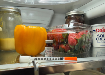 A syringe rests on the top shelf of a fridge.