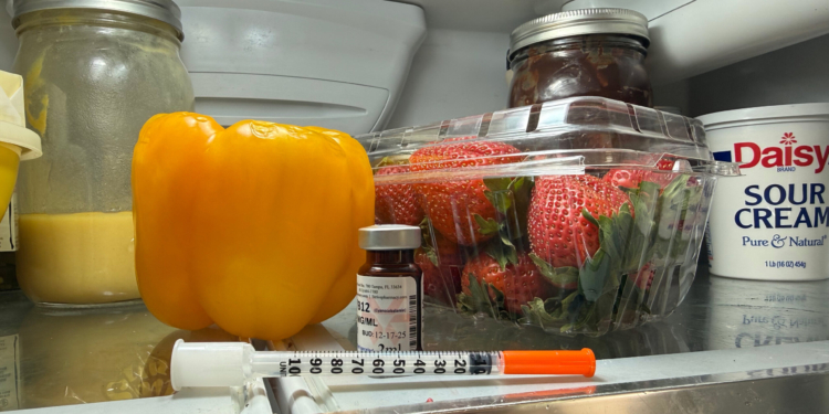 A syringe rests on the top shelf of a fridge.