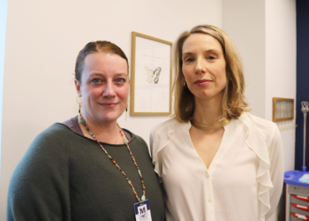 Two women with blonde-ish hair stand side-by-side in a doctor's office.
