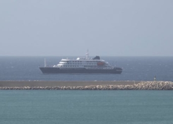 A cruise ship is seen in the water, with a piece of land nearby.