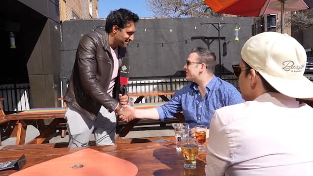 One man with a TV microphone is shaking hands with another man, while a third man looks on.