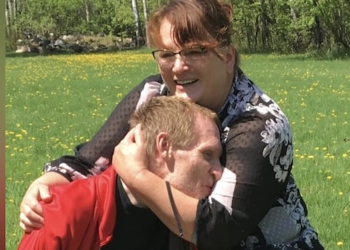 A woman in a red sweater hugging a man with short hair outside.