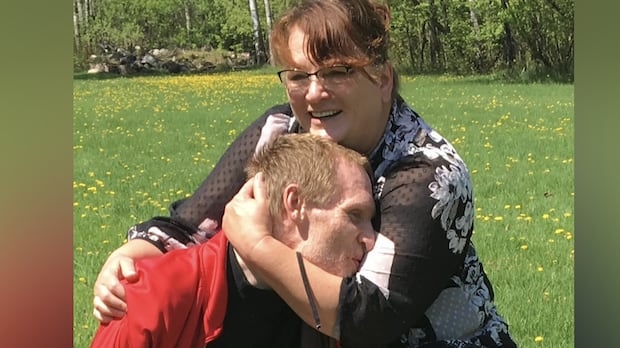 A woman in a red sweater hugging a man with short hair outside.