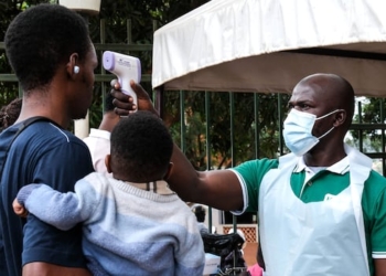 A medical official uses a thermometer to screen a man carrying a child.