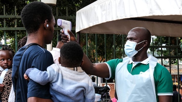 A medical official uses a thermometer to screen a man carrying a child.