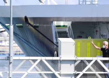 A person on a ship is raising their hand in a wave to someone out of the frame.