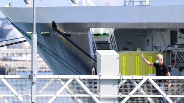 A person on a ship is raising their hand in a wave to someone out of the frame.